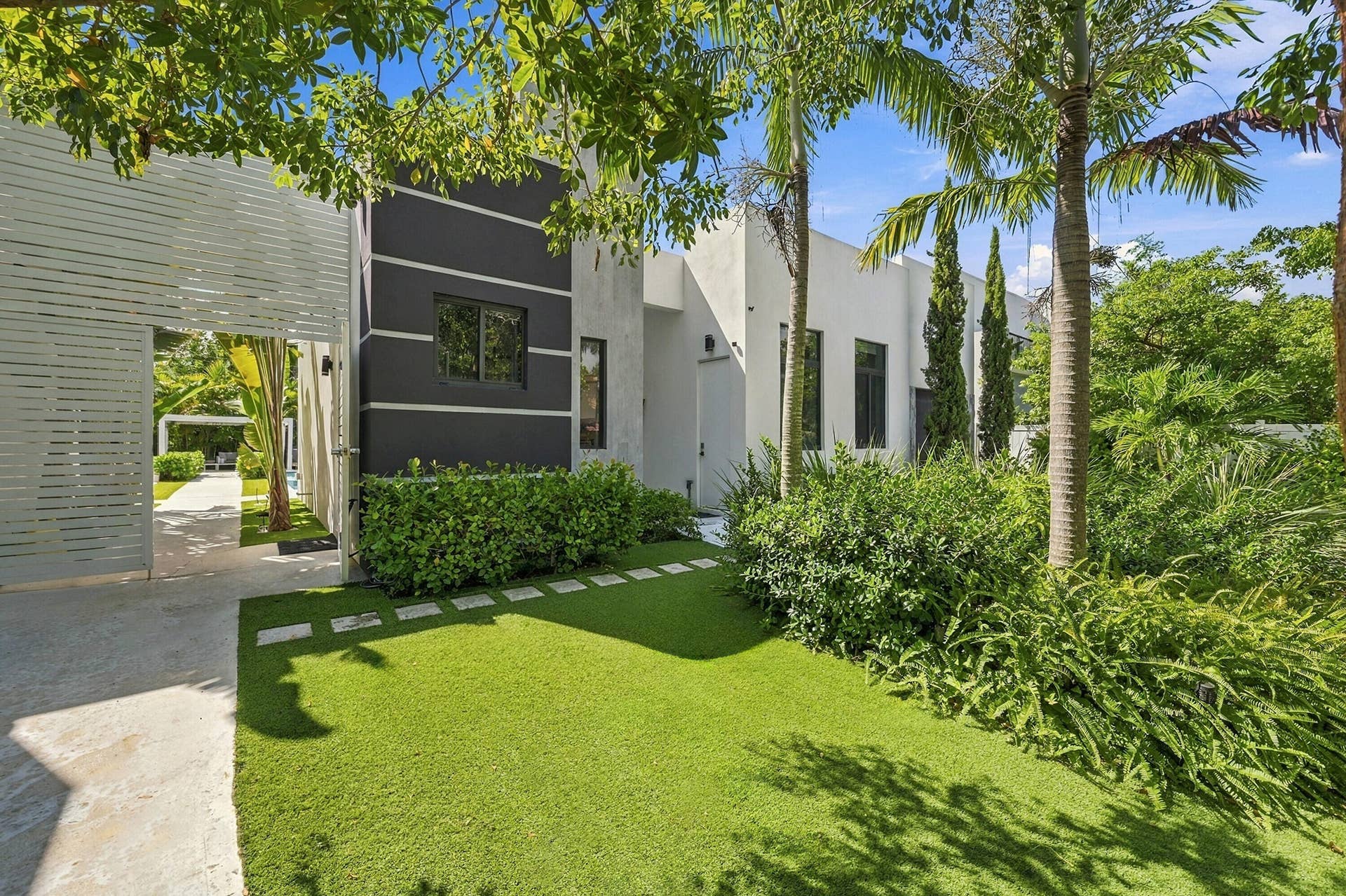110 NE 16TH Place, Fort Lauderdale, FL 33305 Modern exterior featuring a white facade with dark accent panels, square windows, and a manicured lawn with stepping stones
