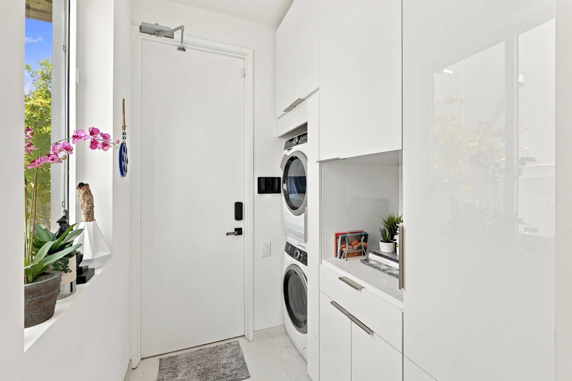 110 NE 16TH Place, Fort Lauderdale, FL 33305 High-gloss white cabinetry, stacked laundry appliances, white countertop, and a window with natural light
