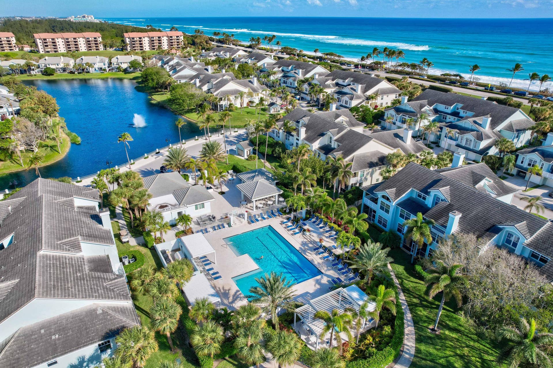 2043 Staysail Lane, Jupiter, Jupiter, FL 33477 Community featuring a large swimming pool, covered outdoor lounge areas, a private lake with fountain, tropical landscaping, and immediate proximity to the ocean