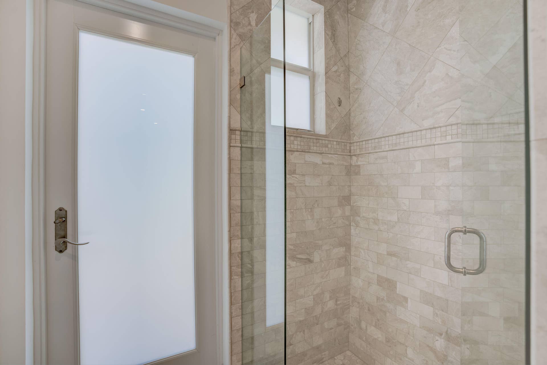 2043 Staysail Lane, Jupiter, Jupiter, FL 33477 Frosted glass panel door with antique brass hardware, clear glass shower enclosure, tiled shower walls with decorative accent band, and an inset window