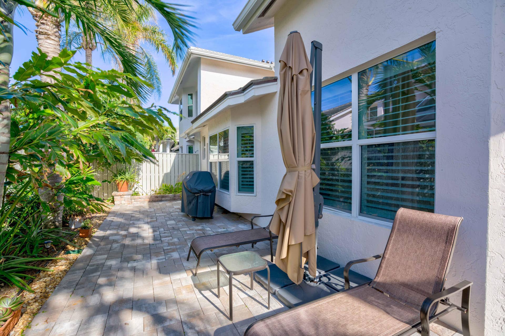 2043 Staysail Lane, Jupiter, Jupiter, FL 33477 Paved patio area with a white stucco exterior, multiple windows with internal blinds, and established tropical landscaping