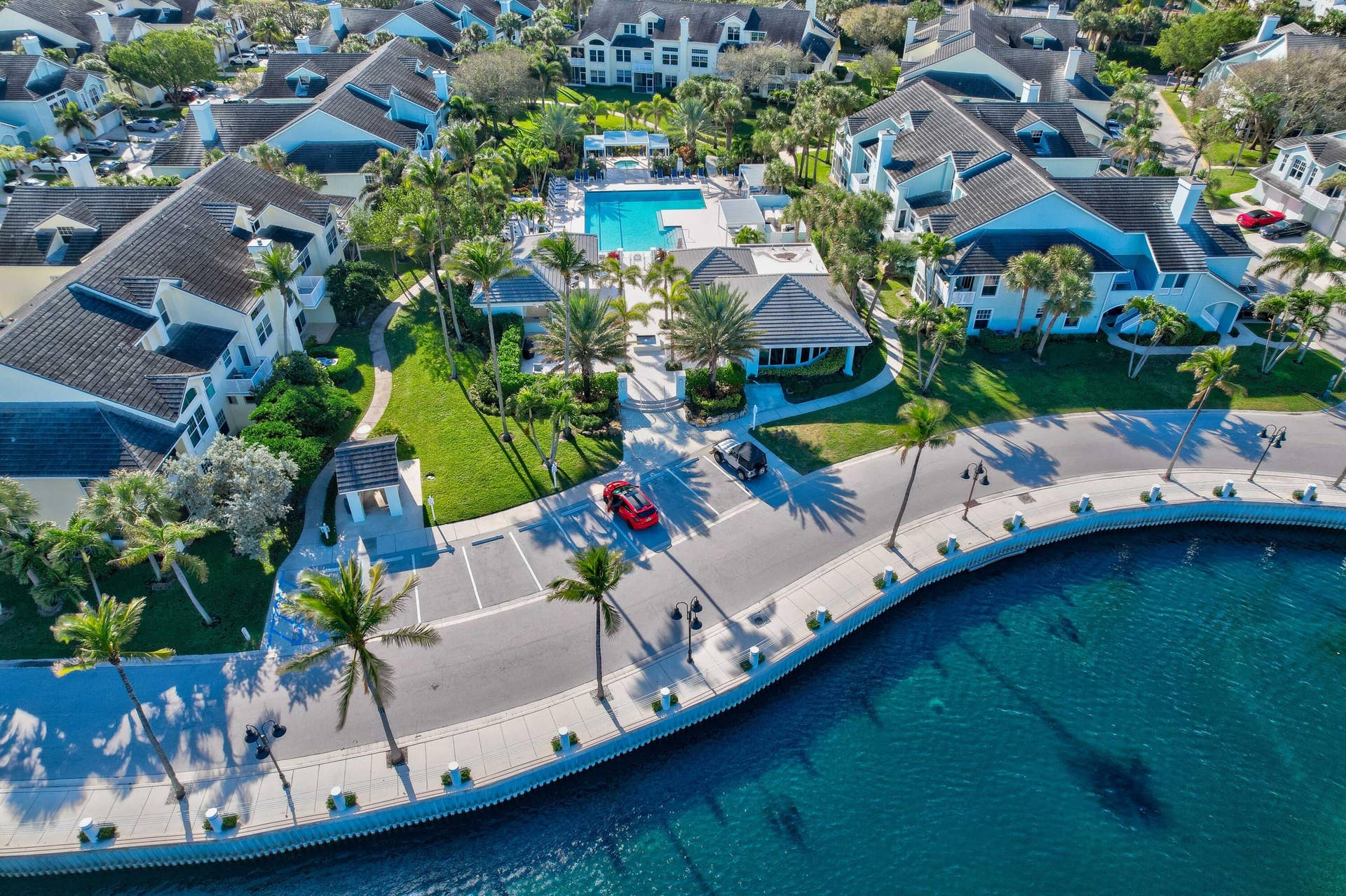 2043 Staysail Lane, Jupiter, Jupiter, FL 33477 Waterfront property featuring a community swimming pool, mature palm trees, manicured landscaping, and a paved walkway along the water