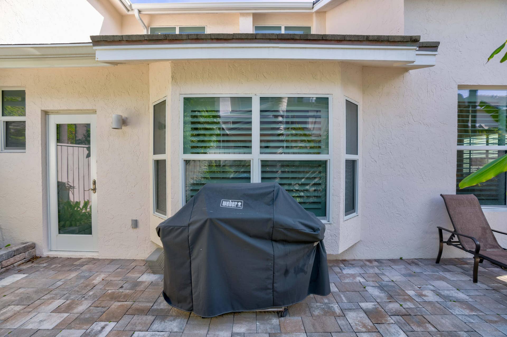 2043 Staysail Lane, Jupiter, Jupiter, FL 33477 Paved patio area with multi-tone pavers, a bay window with plantation shutters, a white exterior door, and stucco siding