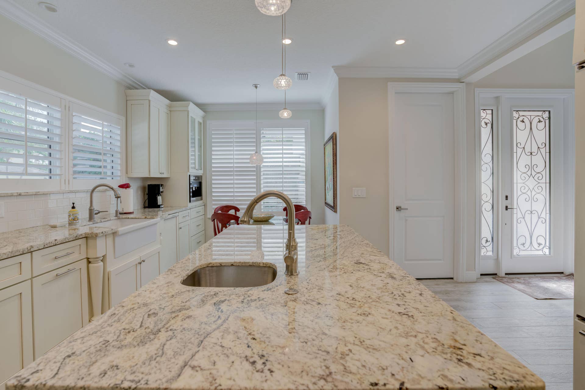 2043 Staysail Lane, Jupiter, Jupiter, FL 33477 Kitchen island with integrated sink, white shaker cabinetry, plantation shutters, recessed lighting, and ornate glass double entry doors