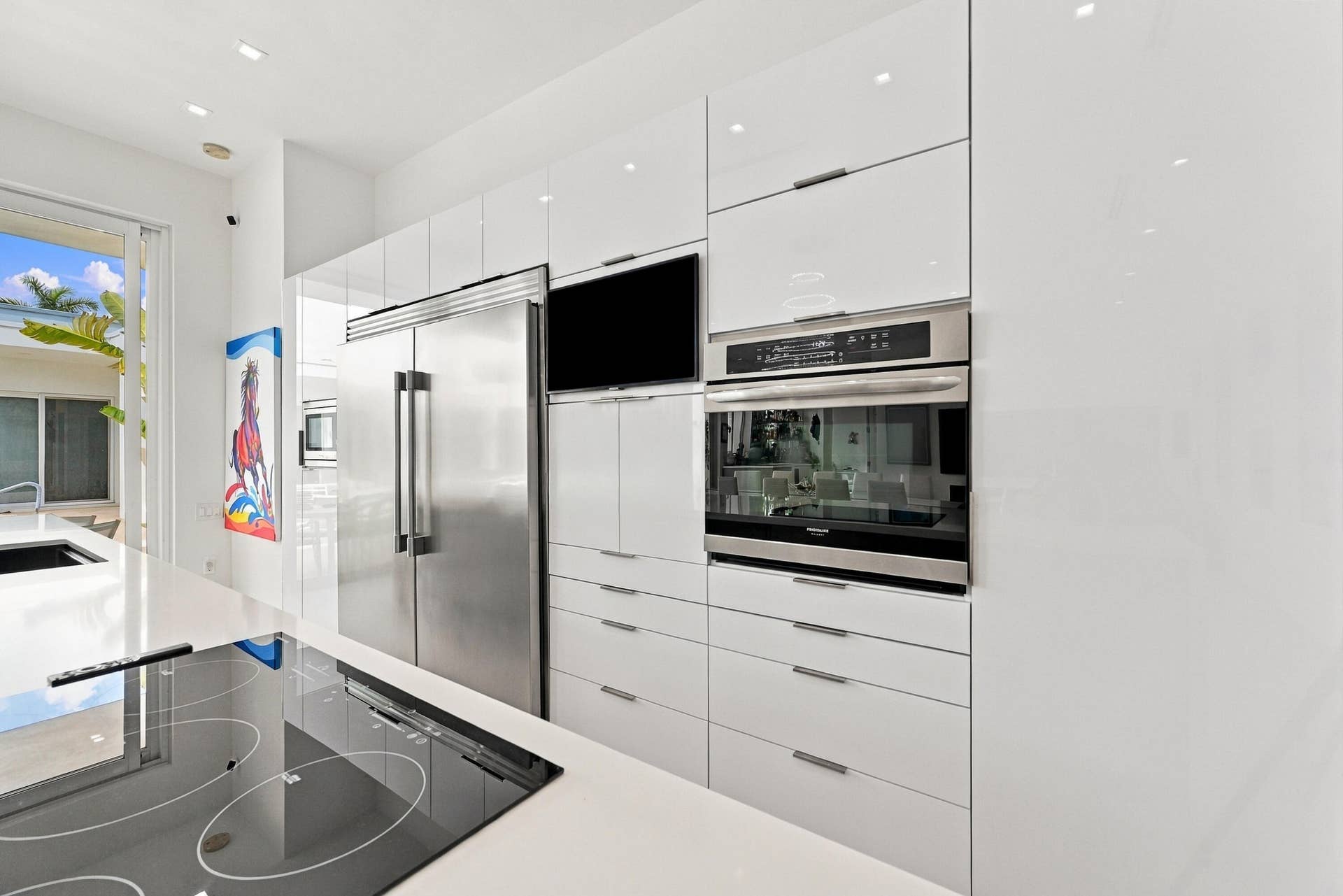 Sleek white cabinetry, integrated stainless steel appliances, and a built-in cooktop complement the kitchen's contemporary design