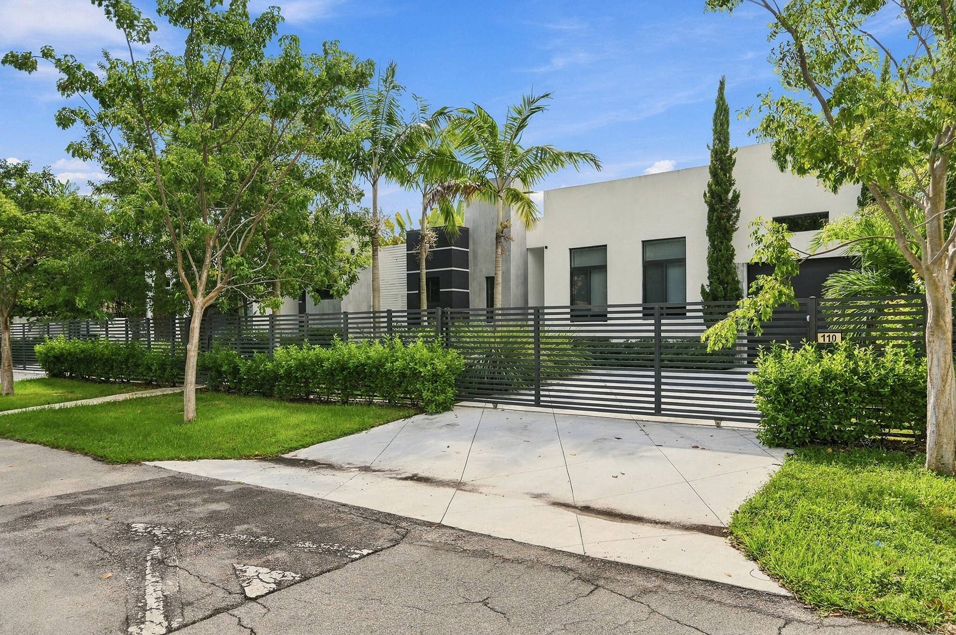 Smooth stucco exterior, horizontal slatted fencing, manicured landscaping, concrete driveway, and established trees