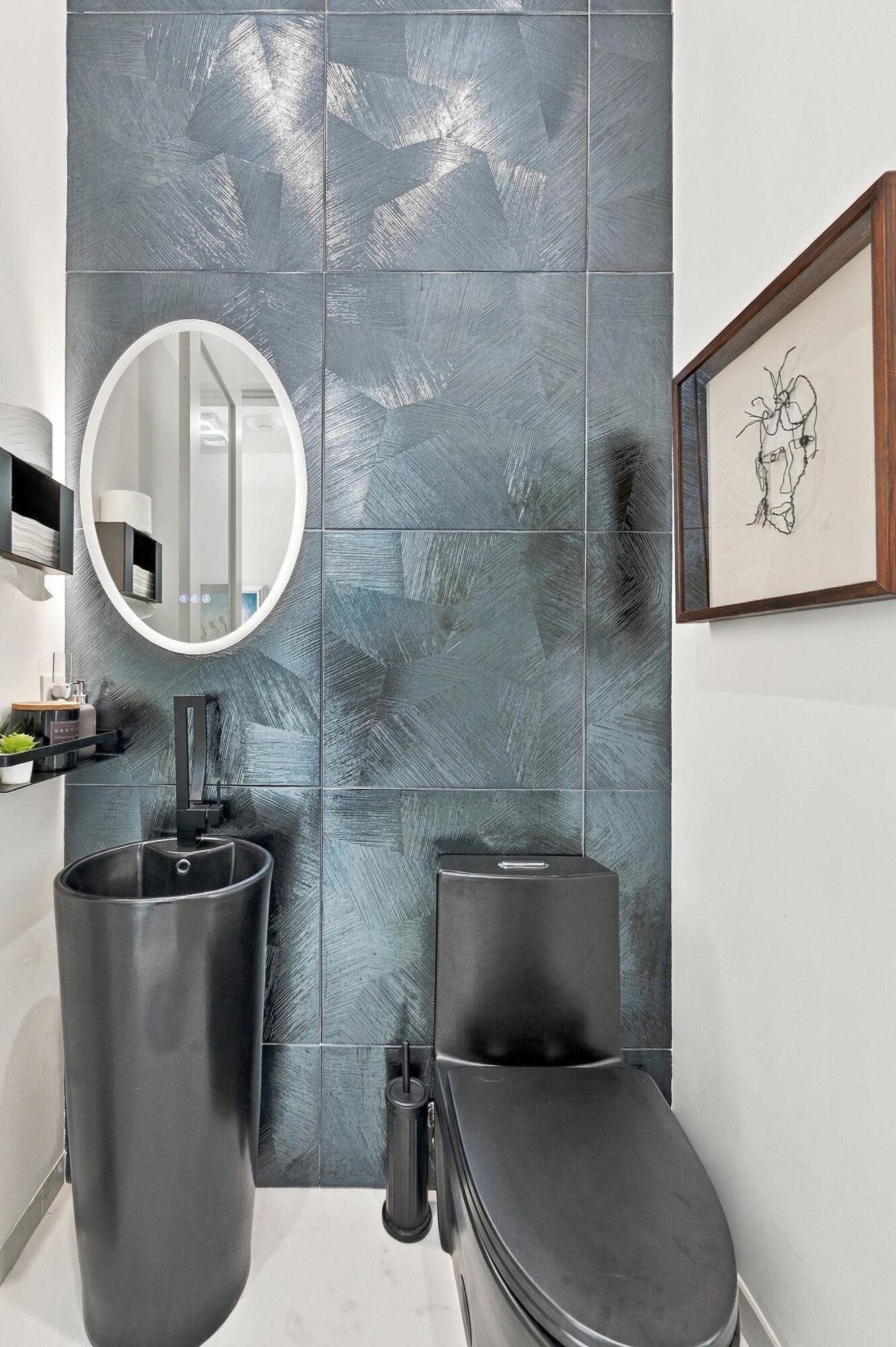 Textured wall tiling, pedestal sink with integrated faucet, contemporary black toilet, and oval-framed mirror