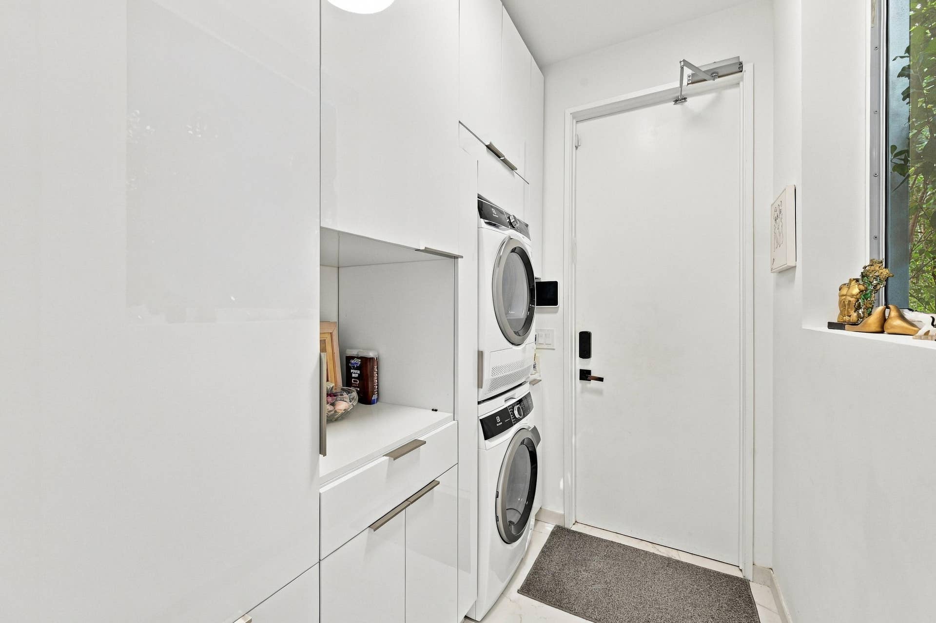 White glossy cabinetry with integrated hardware, stacked washer and dryer, and a fixed pane window