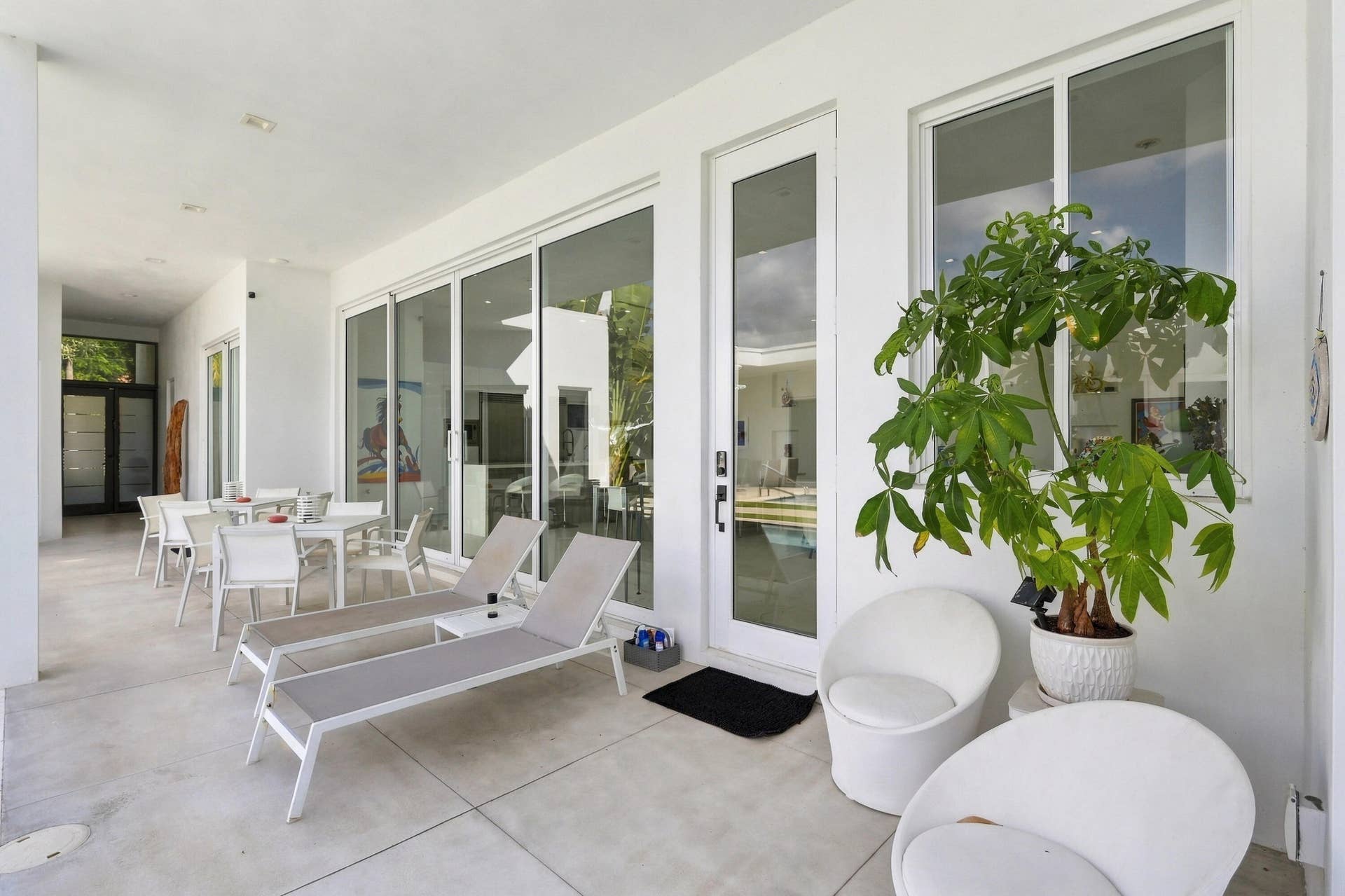 Expansive concrete patio with white exterior walls, multiple floor-to-ceiling glass sliding doors, and a glass-paneled entry door