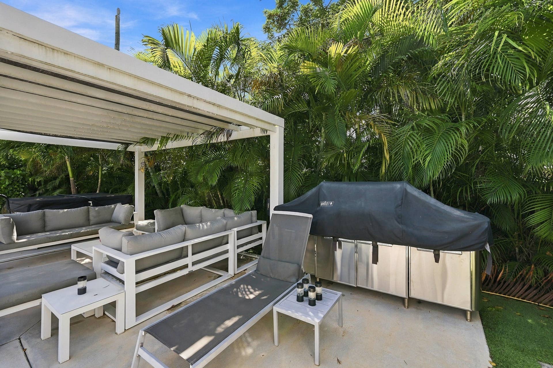 Expansive outdoor patio with a louvered pergola, integrated stainless steel outdoor kitchen, and lush tropical landscaping