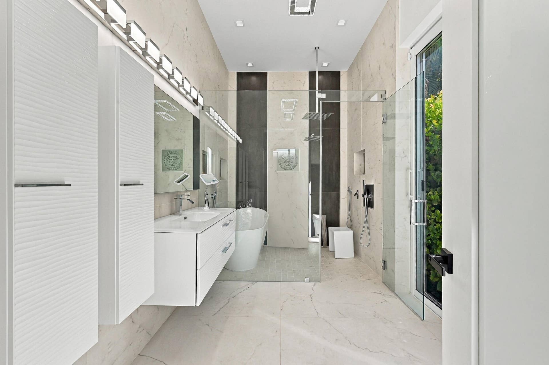 Floating vanity with integrated sink, glass-enclosed shower, freestanding tub, recessed lighting, and large format floor tiles