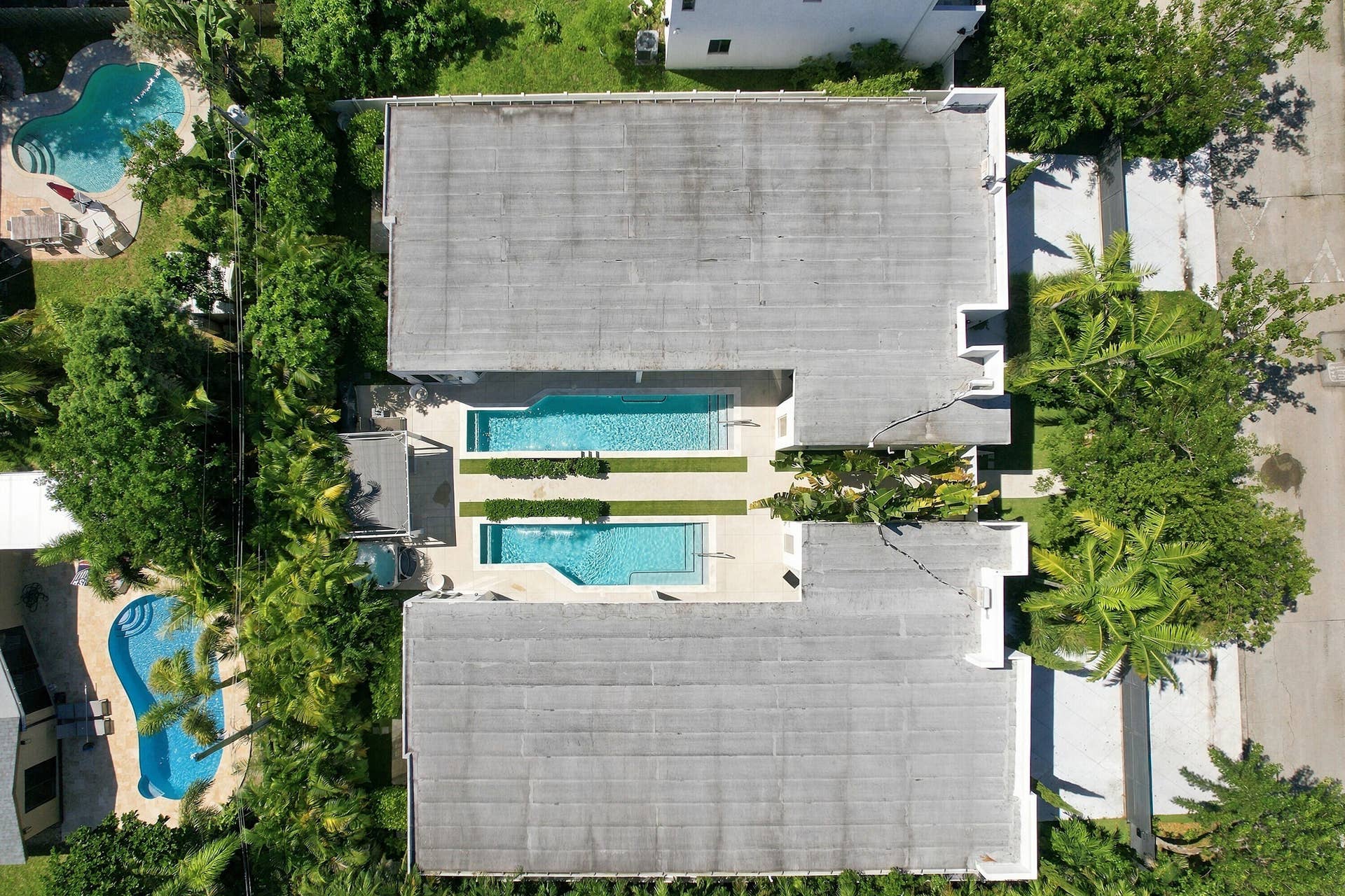 Two rectangular pools with surrounding hardscaping, lush landscaping, and mature trees