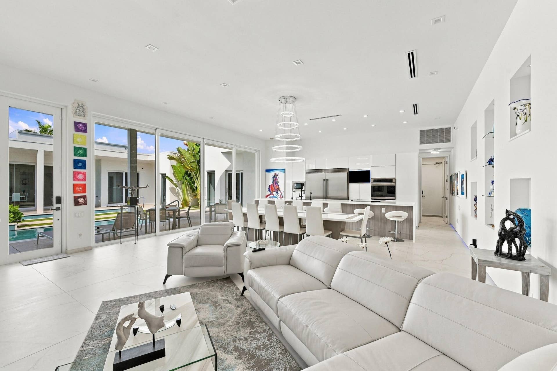 Open-concept living area with large format tile flooring, a modern kitchen featuring built-in stainless steel appliances, a kitchen island with seating, and integrated wall display niches
