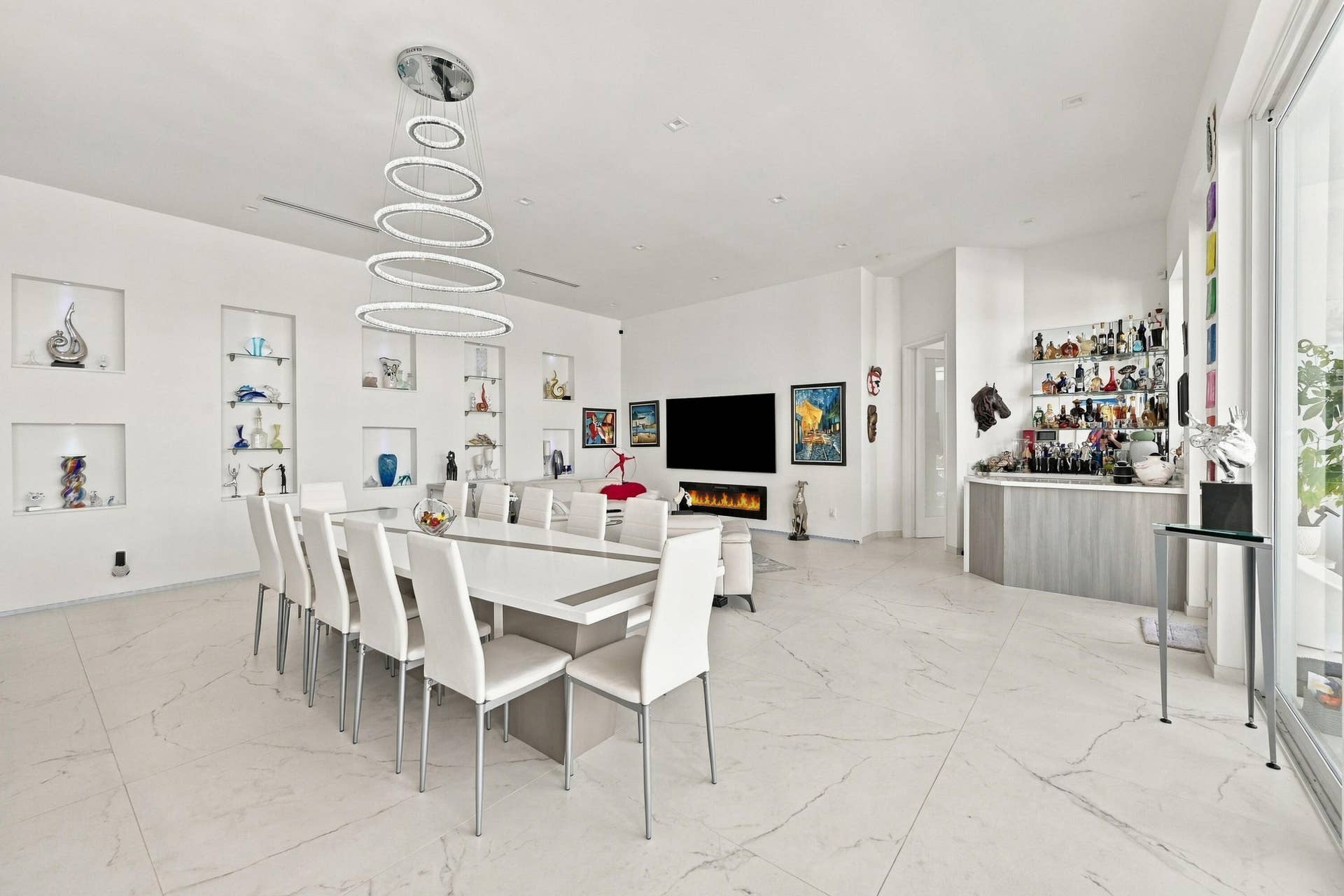 Open-concept living space with large format tile flooring, a built-in wet bar, recessed wall niches, and a linear fireplace