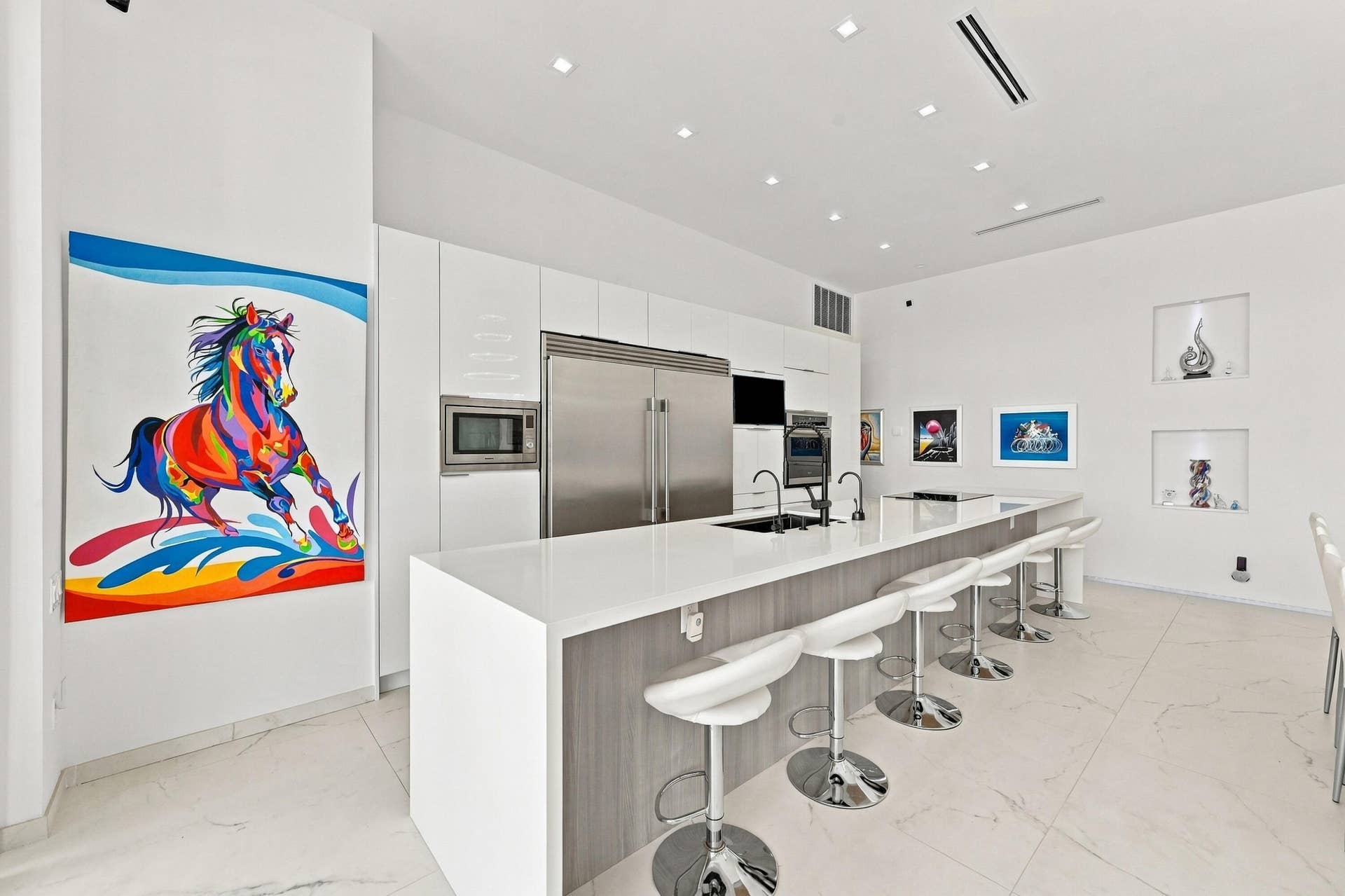 Modern kitchen featuring integrated stainless steel appliances, a large island with a waterfall countertop, recessed lighting, and built-in display niches
