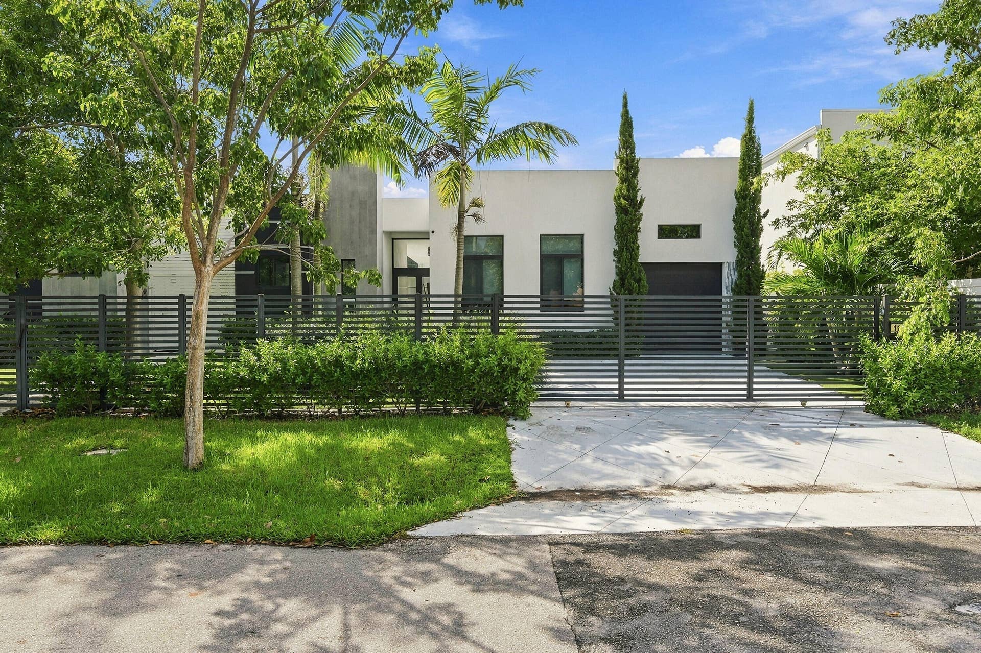Modern exterior with a white stucco facade, black horizontal slat fencing, integrated garage door, tall narrow windows, and a concrete driveway