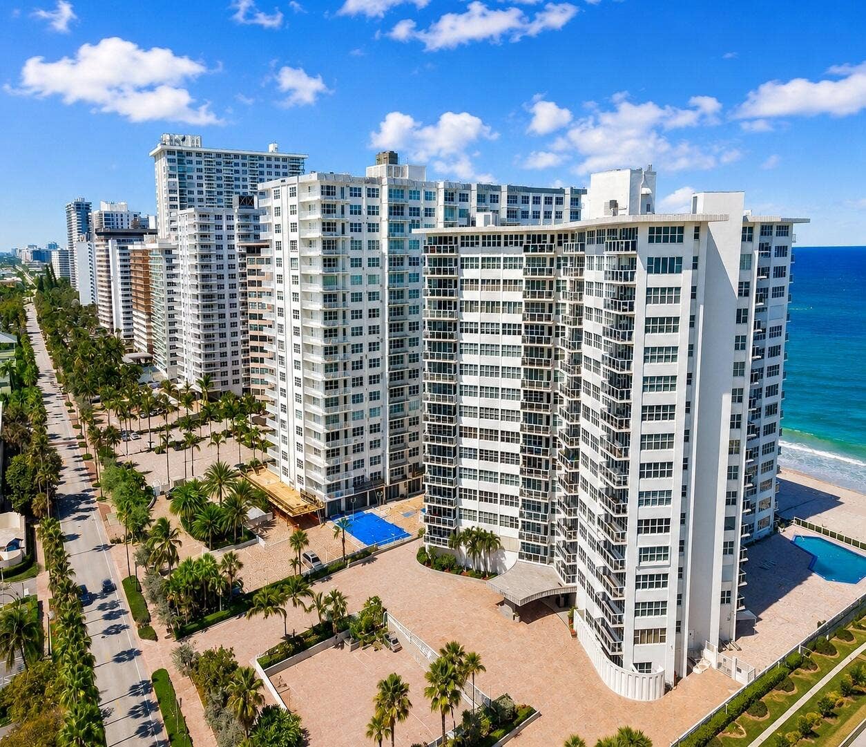 High-rise coastal building with multiple balconies, an adjacent swimming pool, and a dedicated entrance driveway