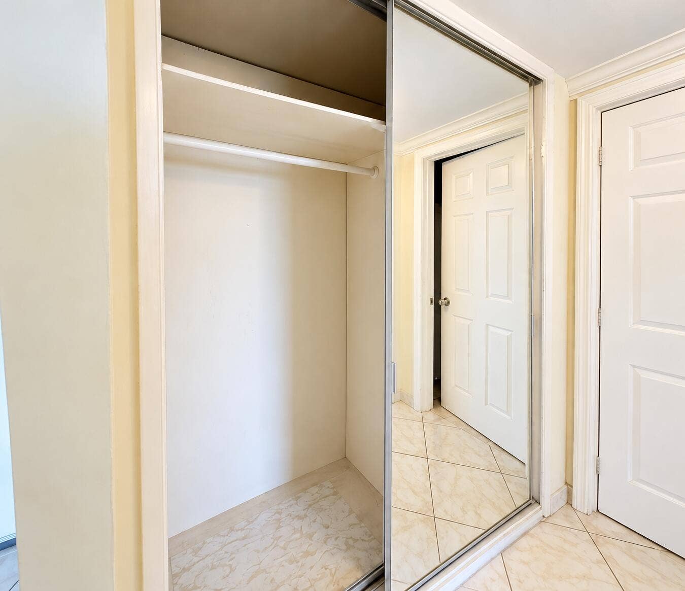 Built-in closet with hanging rod and upper shelf, featuring sliding mirrored doors and a light-toned tile floor