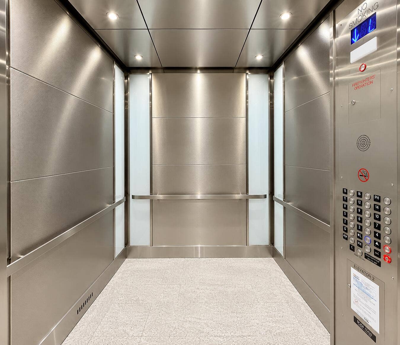 Stainless steel interior paneling, recessed ceiling lighting, a full-height control panel, light-colored flooring, and integrated handrails