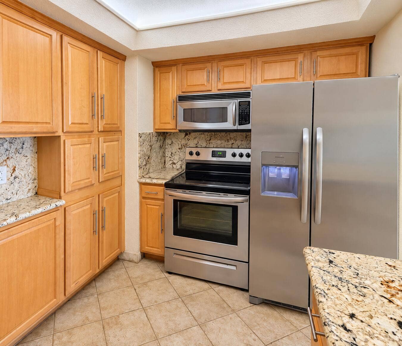 Kitchen featuring stainless steel appliances, wood cabinetry, stone countertops, stone backsplash, and tiled flooring