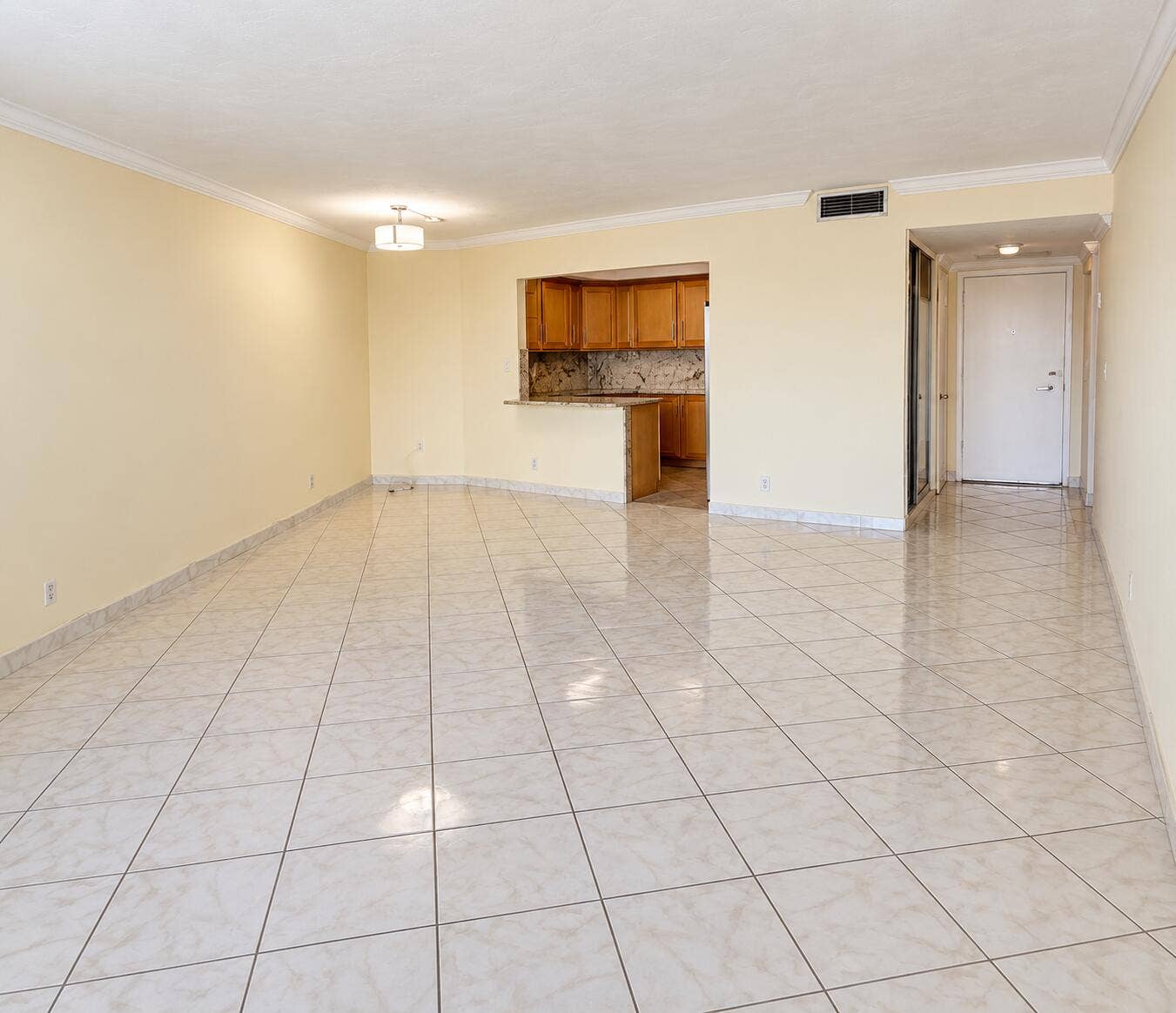 Spacious room with large format tile flooring, crown molding, and an integrated kitchen pass-through with stone countertop