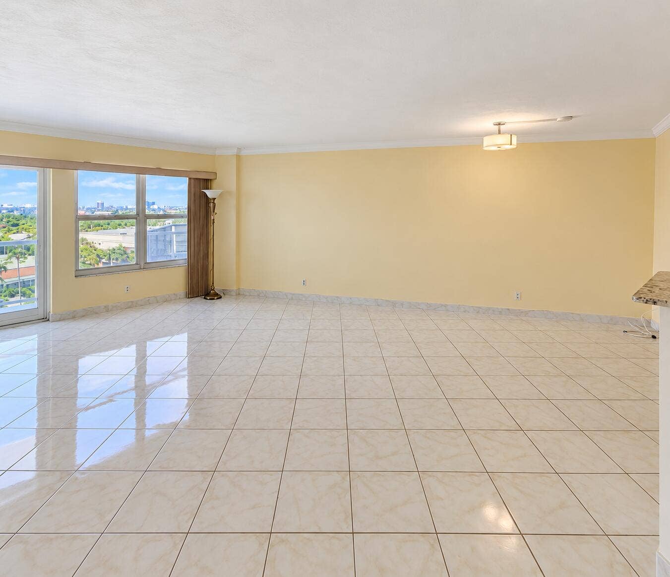 Expansive living area featuring large tile flooring, a wide window with city and green space scenery, and a semi-flush ceiling light fixture