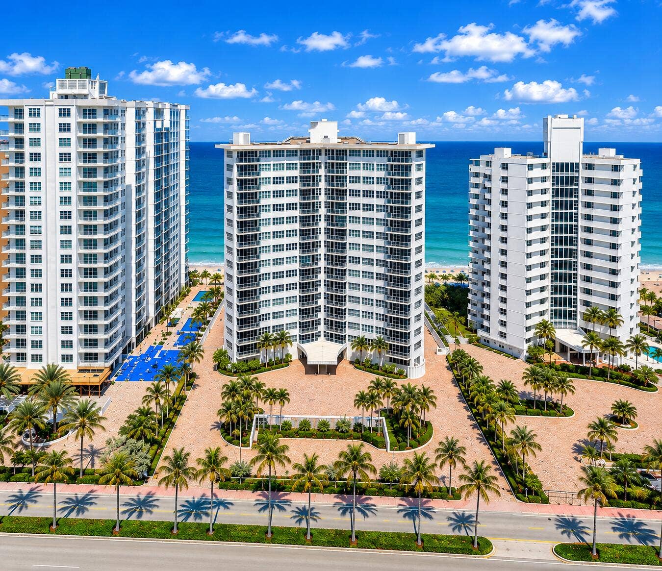 High-rise coastal building featuring multiple balconies, a paver driveway, and mature palm trees