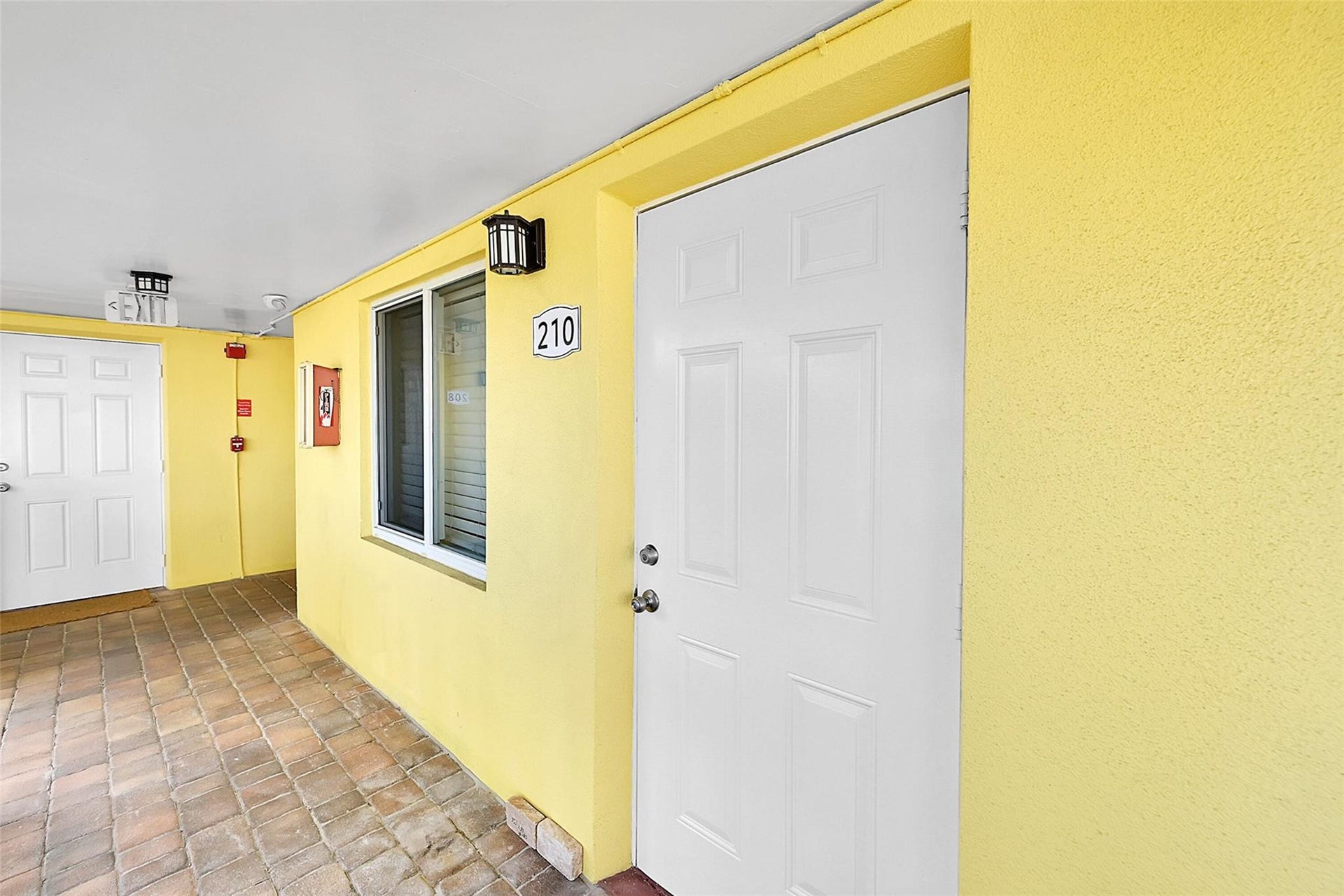 2655 NE 8th Avenue, #Apt 210, Wilton Manors, FL 33334 Textured exterior wall finish, white paneled door, exterior wall sconce, and unit number 210