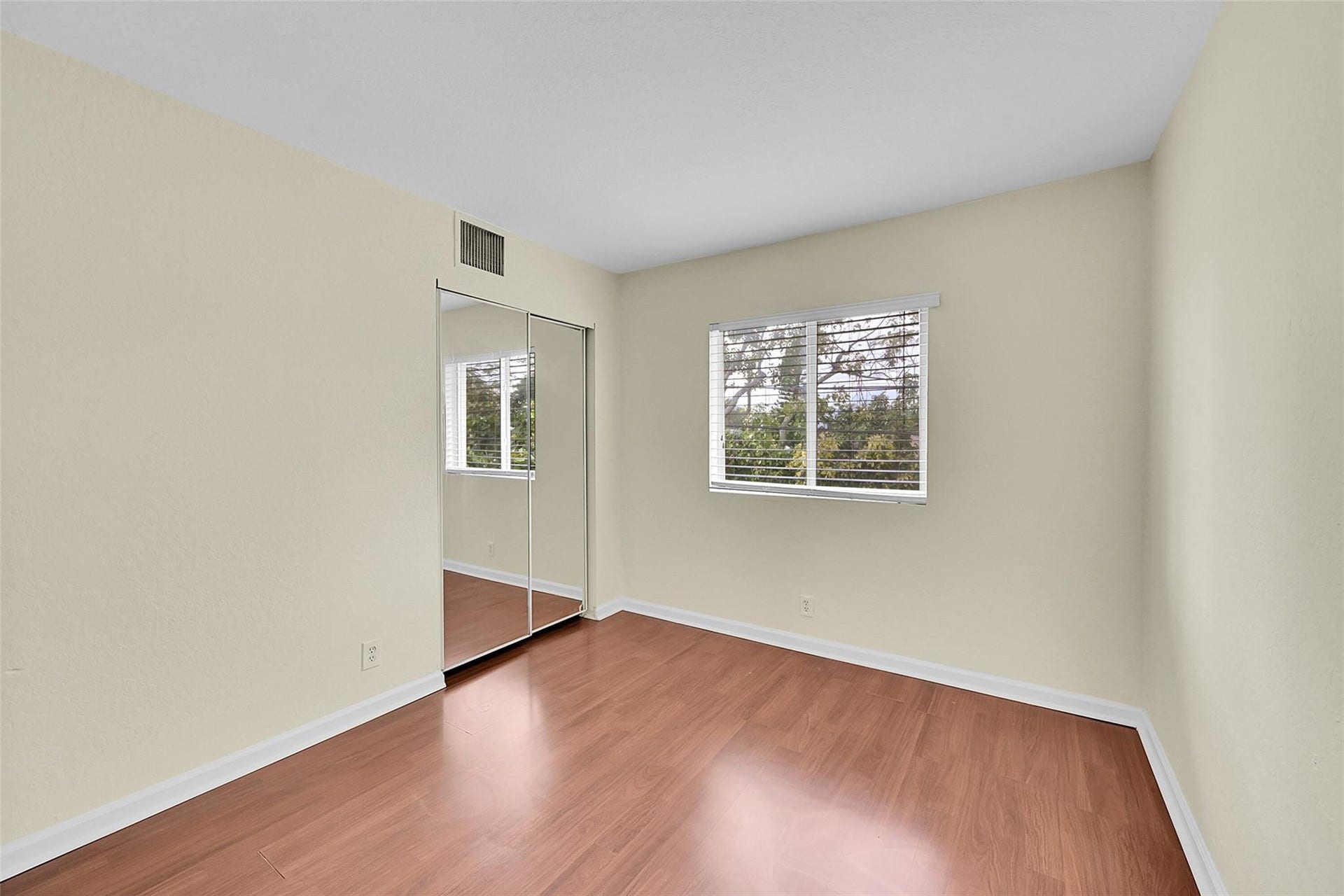 2655 NE 8th Avenue, #Apt 210, Wilton Manors, FL 33334 Wood-finish flooring throughout, light-toned wall paint, mirrored closet doors, and window with horizontal blinds