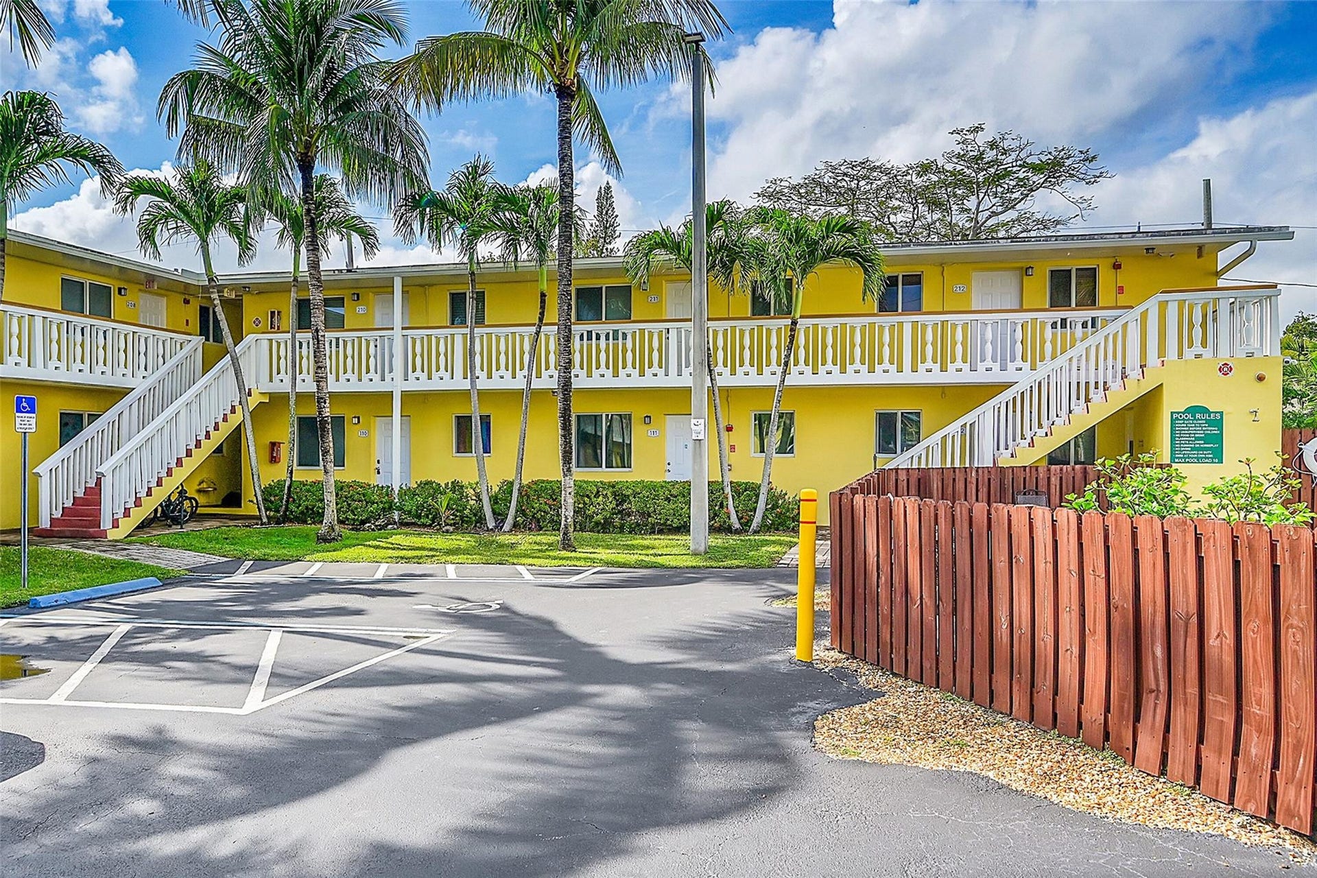 2655 NE 8th Avenue, #Apt 210, Wilton Manors, FL 33334 Two-story building with bright yellow exterior, multiple white-railed staircases, and mature palm trees