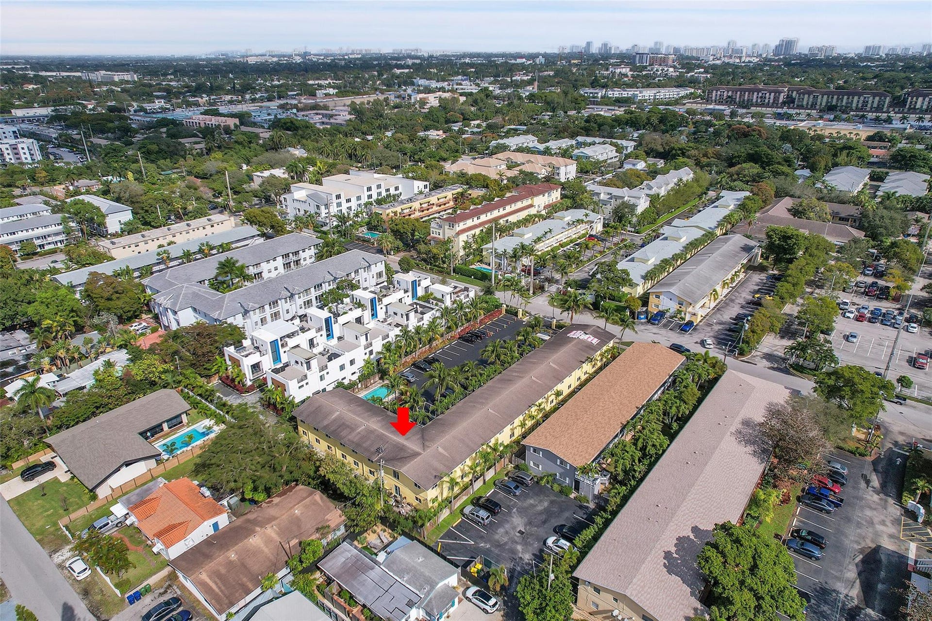 2655 NE 8th Avenue, #Apt 210, Wilton Manors, FL 33334 Property featuring a multi-story structure with a flat roofline, surrounded by mature trees, paved parking areas, and adjacent residential and commercial buildings