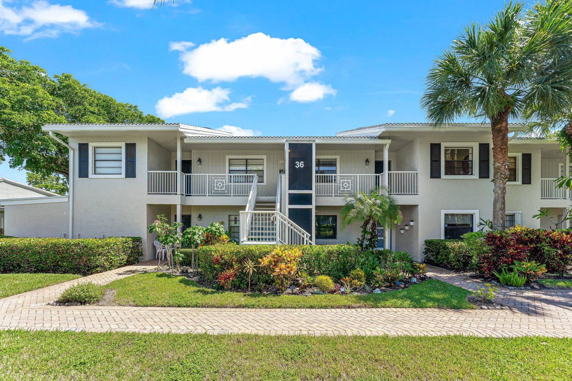 Two-story stucco building with balconies featuring white railings, black louvered shutters, and a tiled roof