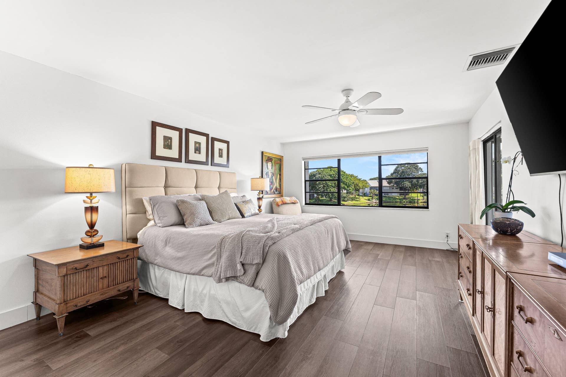 Wood-finish flooring throughout, large window with outdoor landscape, ceiling fan with integrated lighting, and a neutral color palette