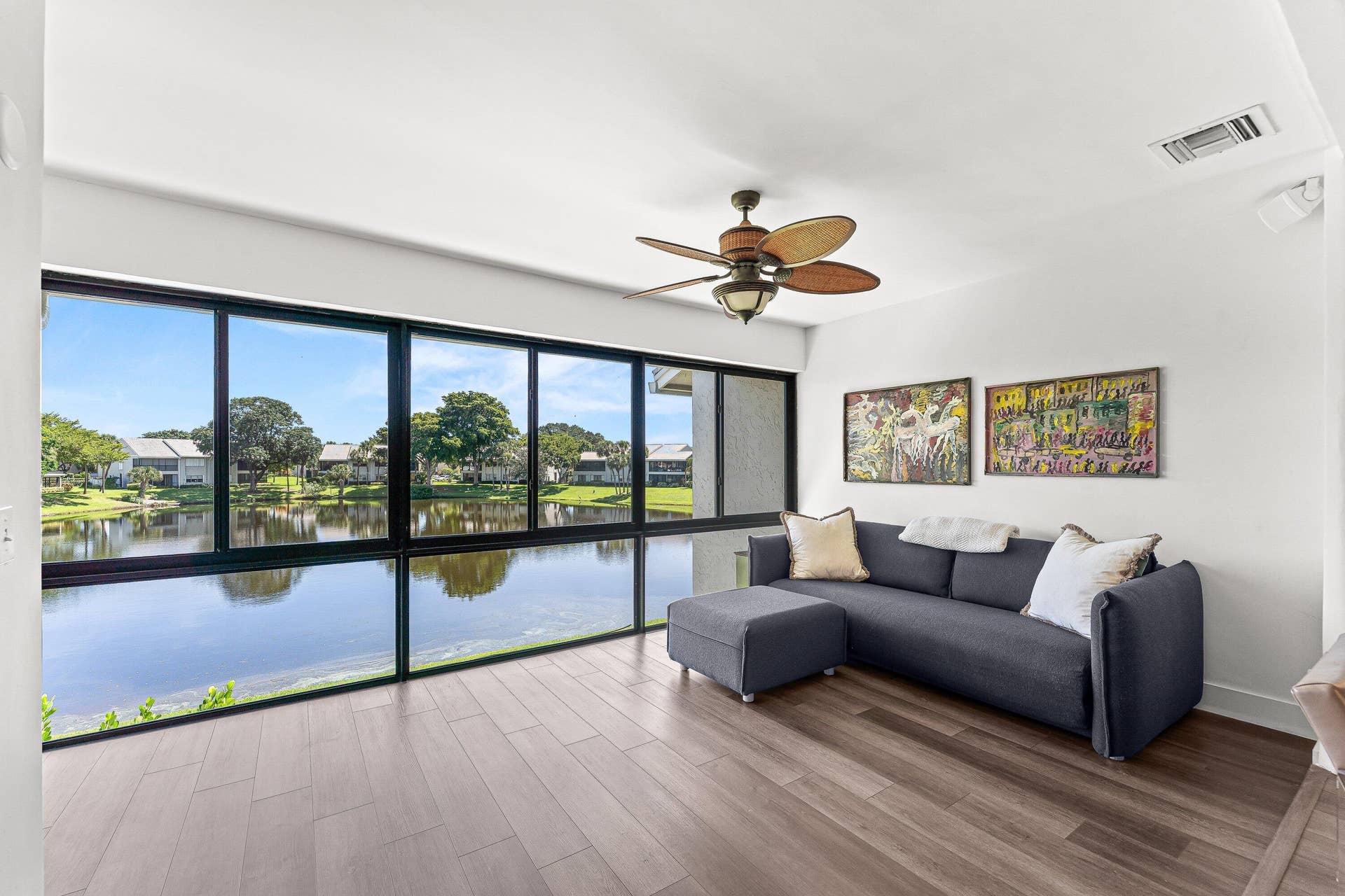 Expansive window wall with a water backdrop, wood-finish flooring, and a ceiling fan with integrated lighting