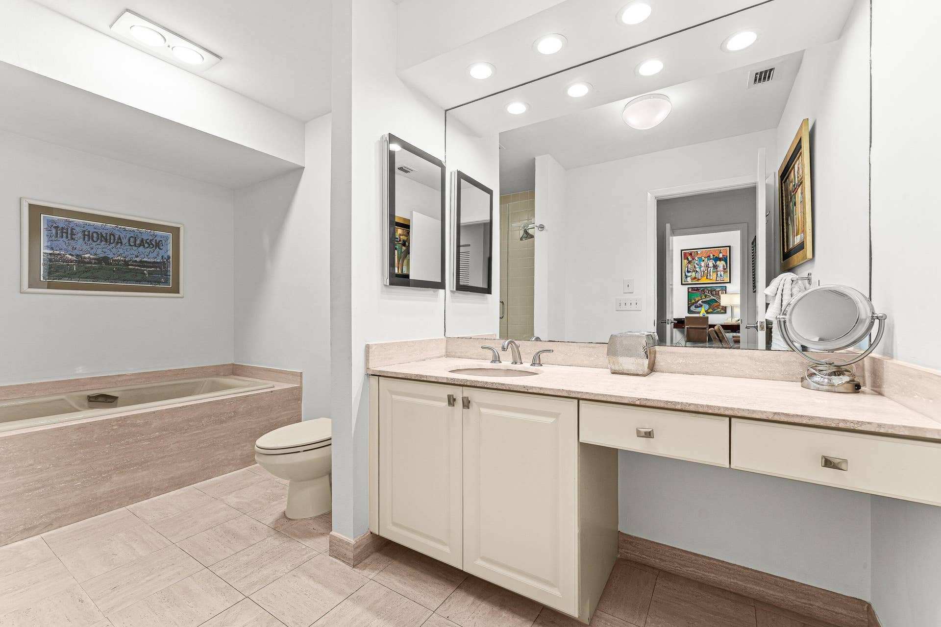 Spacious bathroom featuring a built-in soaking tub, a vanity with a single sink, an integrated makeup counter, and a large wall-mounted mirror