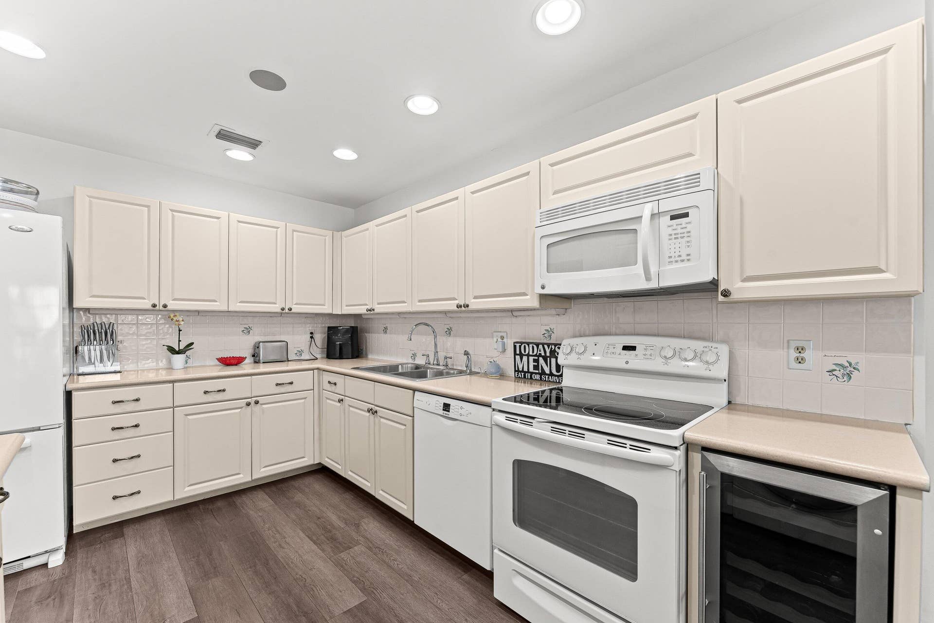 Kitchen featuring wood-finish flooring, recessed lighting, white cabinetry, integrated stainless steel beverage cooler, and white appliances