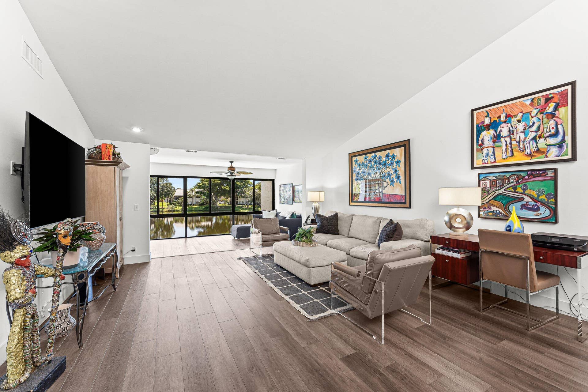 Spacious living area featuring wood-finish flooring, vaulted ceilings, and large impact-rated windows overlooking a water feature
