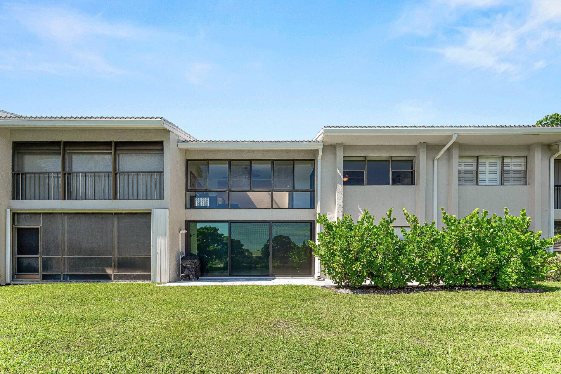 Two-story structure featuring a stucco exterior with multiple large windows, a screened enclosure, and a ground-level patio area