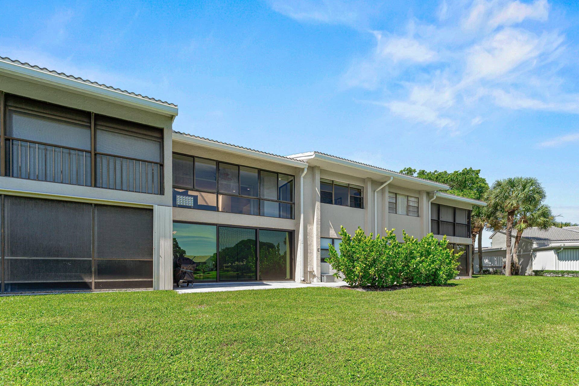 Expansive green lawn, mature palm trees, large window panels, screened balcony, and enclosed patio