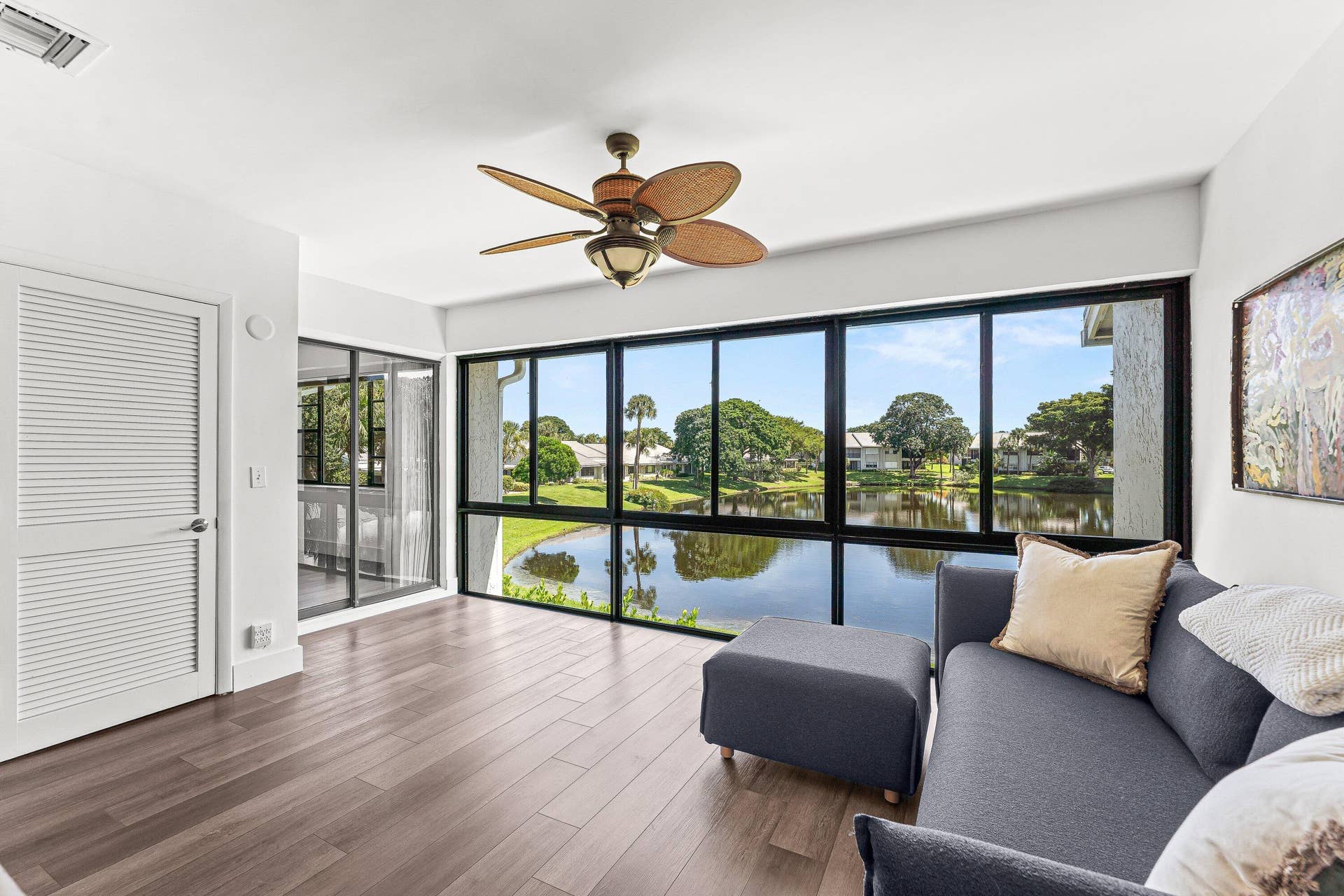 Expansive windows showcasing a water feature and lush landscaping, wood-finish flooring, and a ceiling fan with integrated lighting