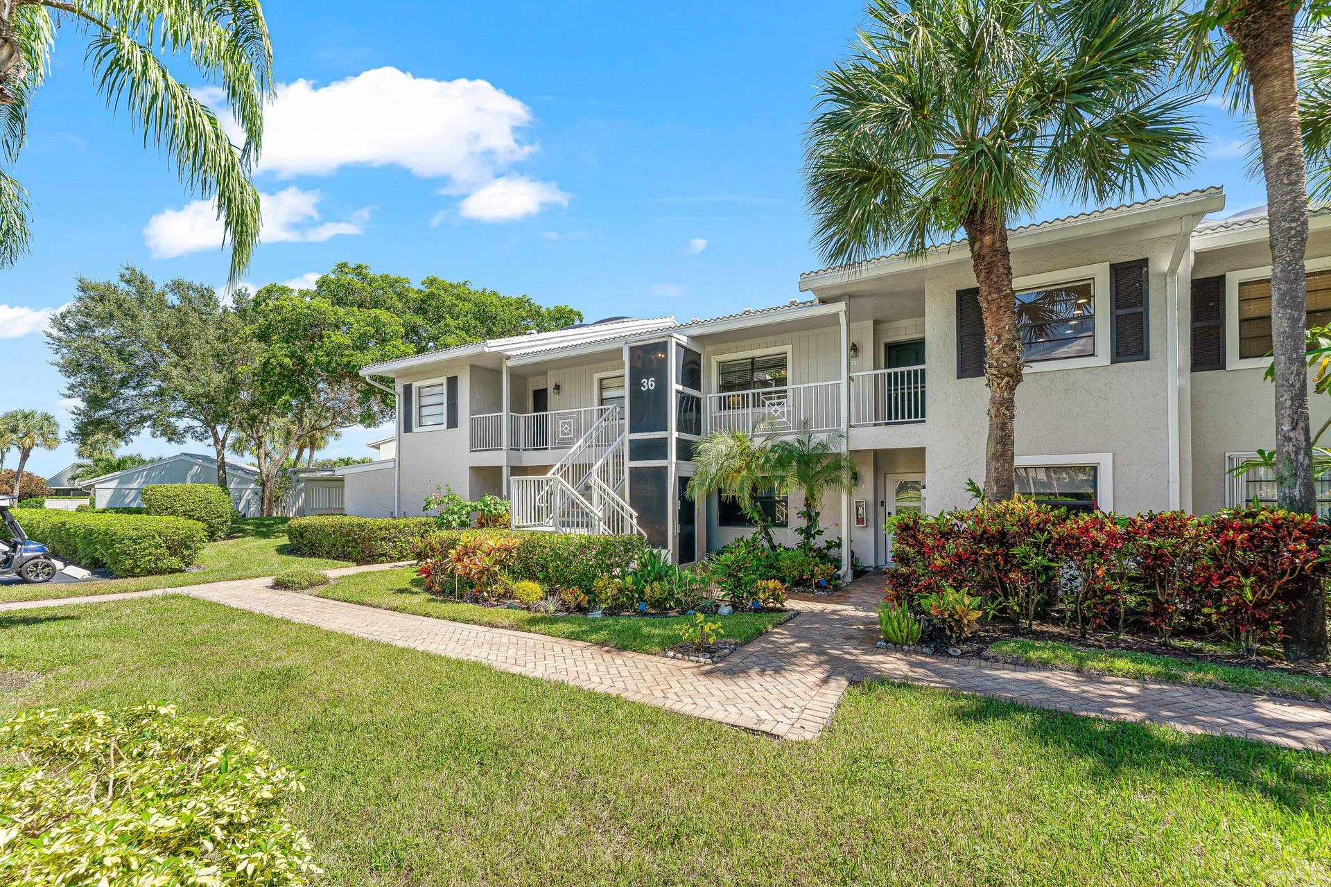 Exterior featuring painted stucco, multiple balconies, a brick paver pathway, mature tropical landscaping, and a manicured lawn