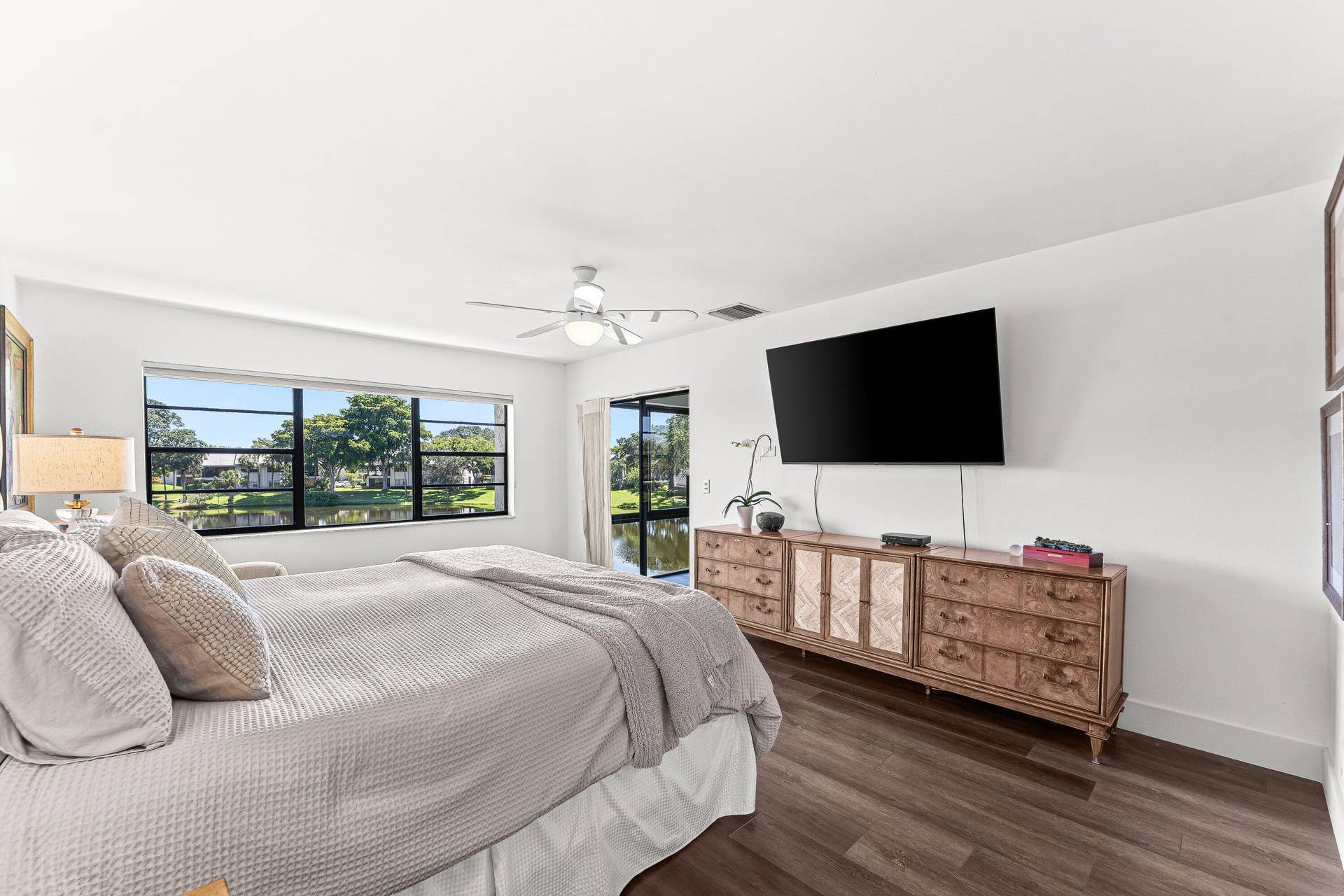 Panoramic windows, wood-finish flooring, ceiling fan, white walls, and built-in wall-mounted television