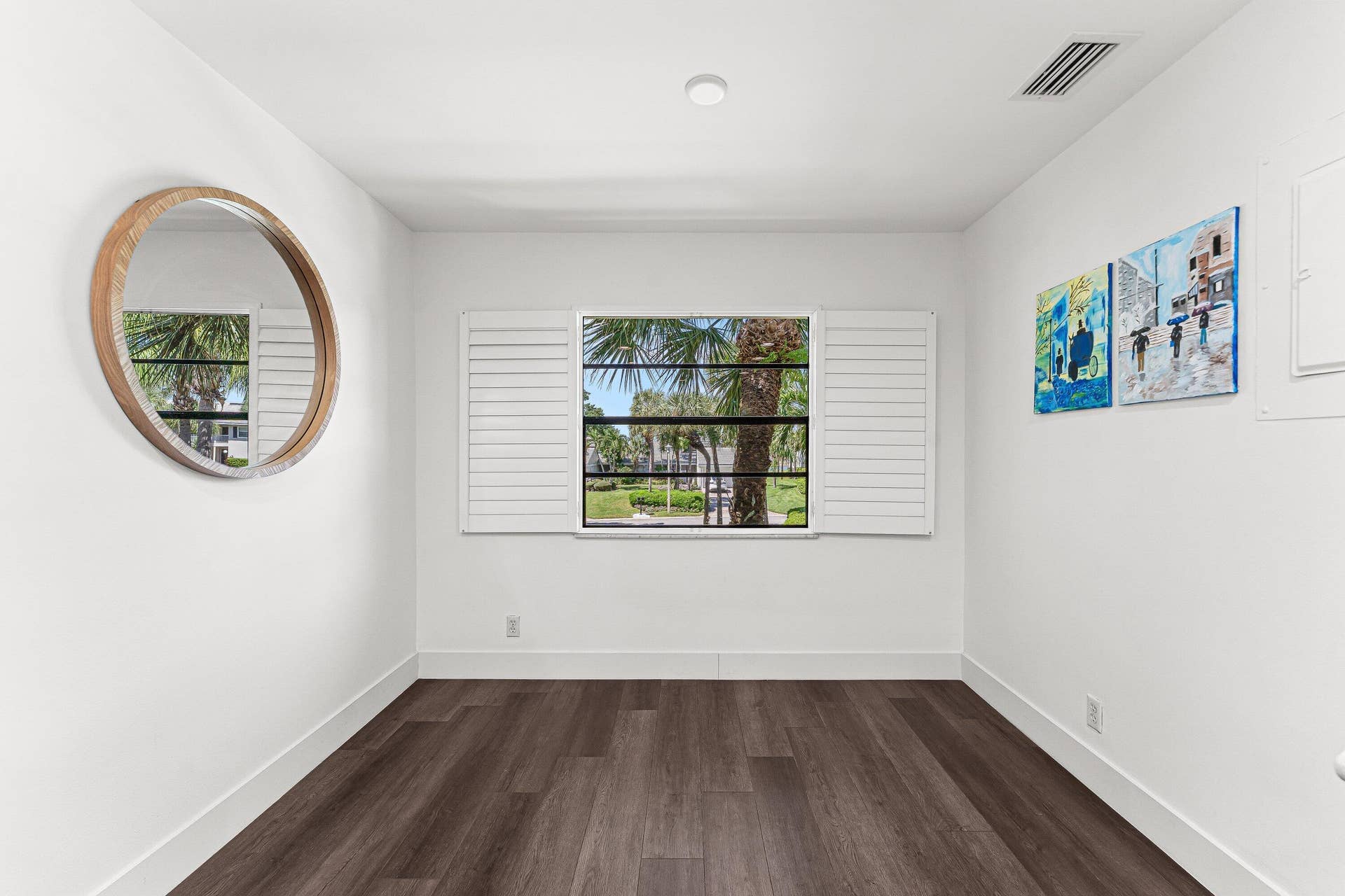 White interior walls featuring wood-finish flooring, a single window with white plantation shutters, and a recessed ceiling light
