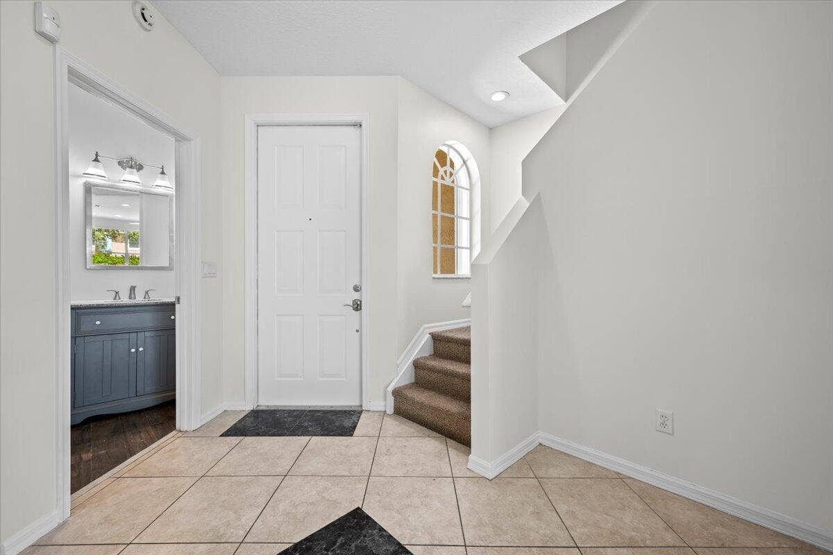 Bright entryway with tile flooring, staircase, and access to the kitchen.