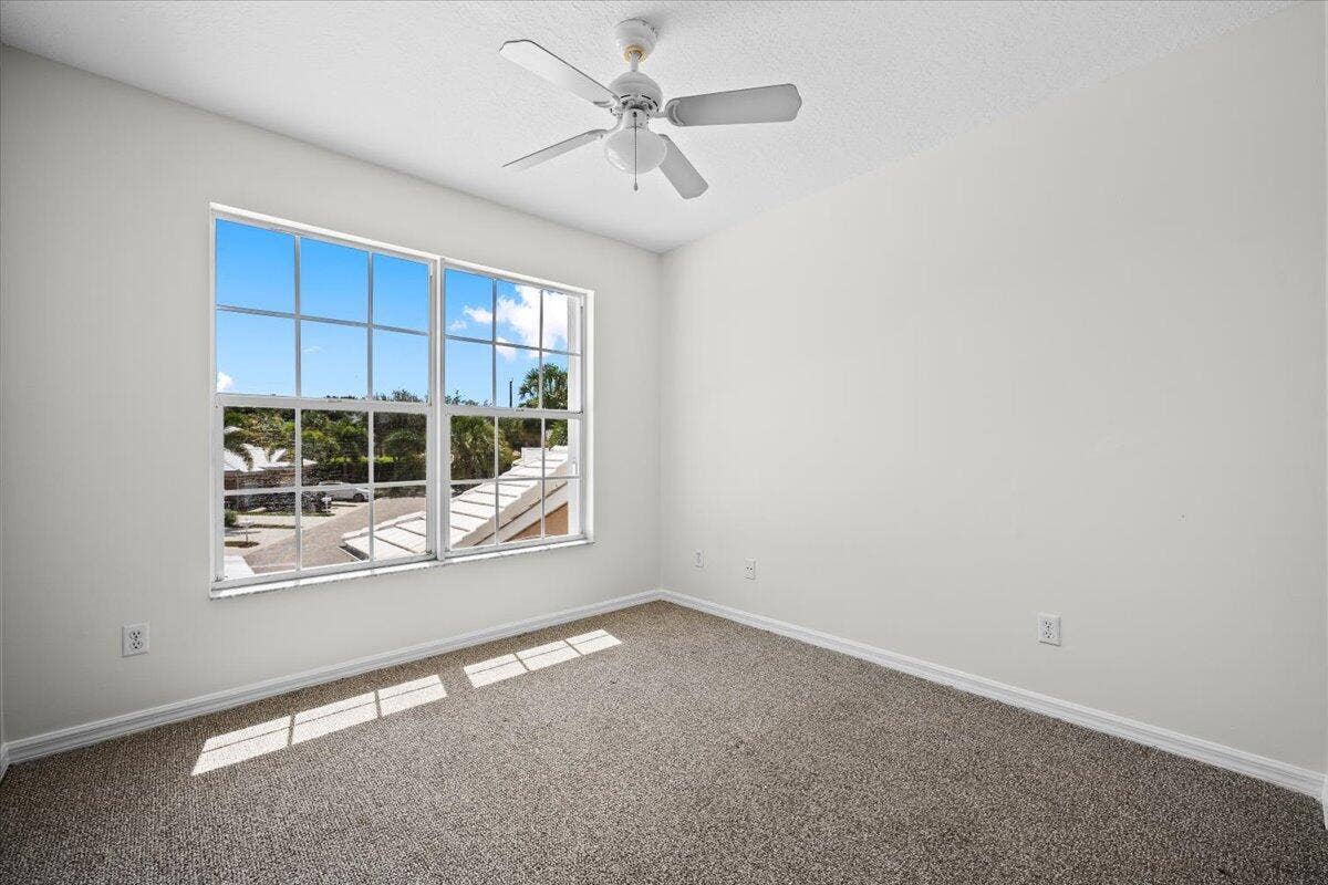 Bright bedroom with carpeting, ceiling fan, and a large window providing natural light.