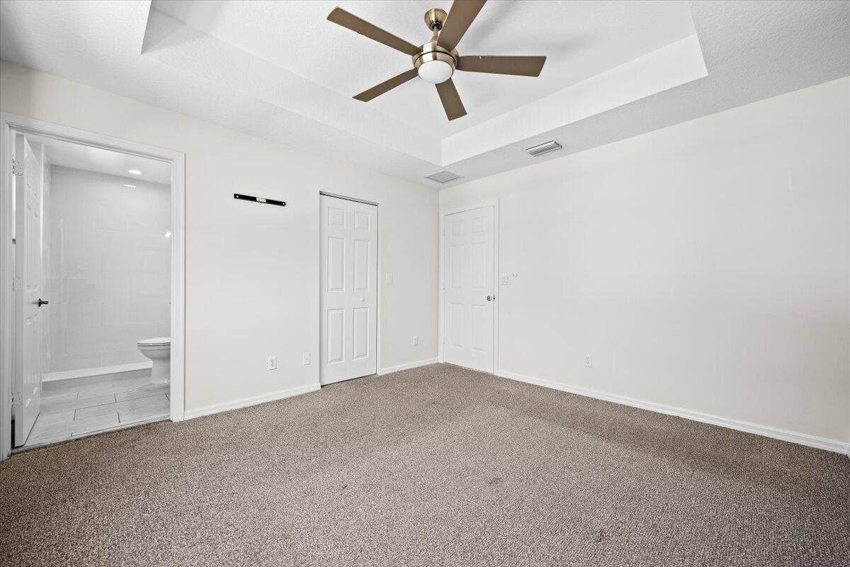 Spacious primary suite with a tray ceiling, ceiling fan, and natural light.