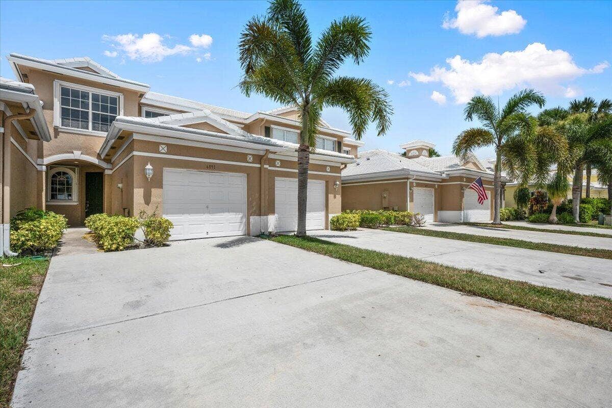dditional view of the home featuring palm trees, landscaping, and a spacious driveway.