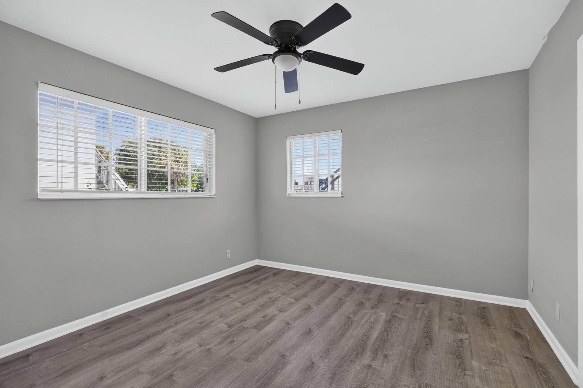 405 SOUTHWIND Drive, #3, North Palm Beach, FL 33408 Neutral-toned room featuring wood-finish flooring, matte black ceiling fan with integrated lighting, and multiple windows with horizontal blinds