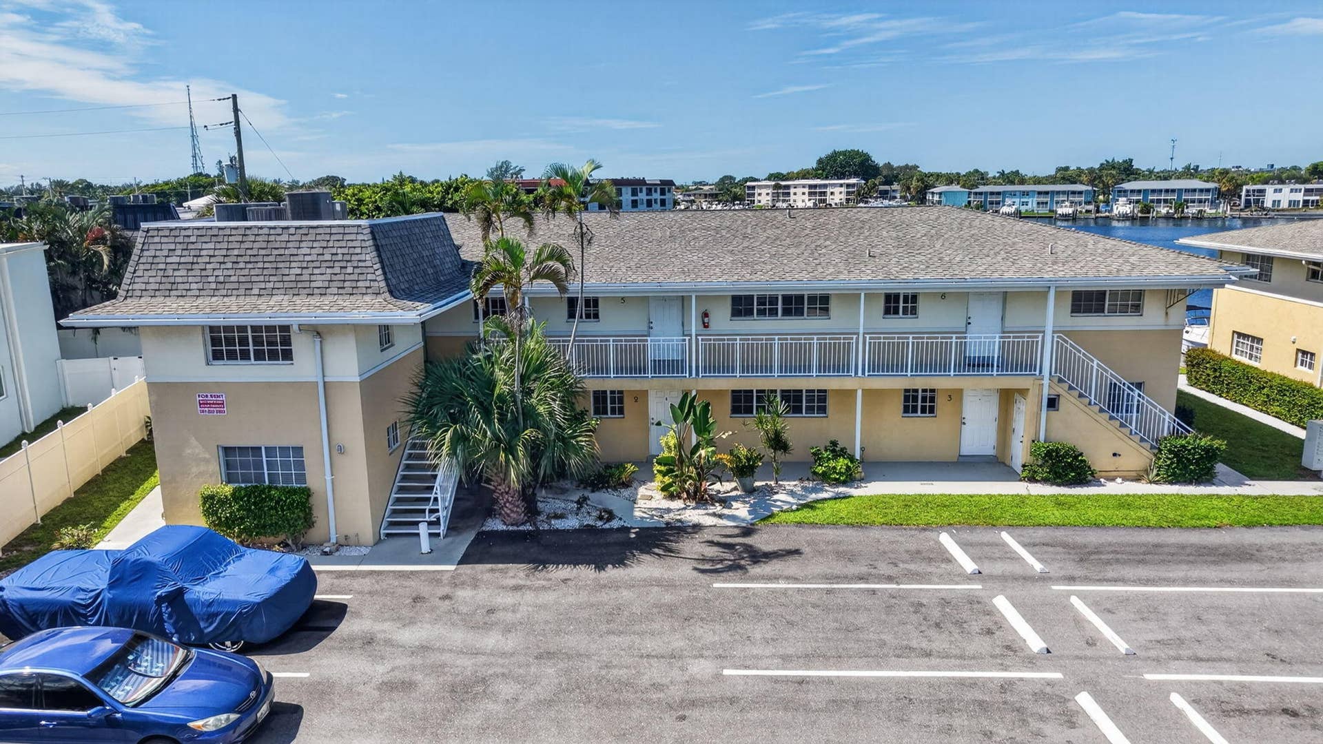 405 SOUTHWIND Drive, #3, North Palm Beach, FL 33408 Multi-story building with a shingled mansard roof, exterior metal balcony railing, paved parking area, and water frontage