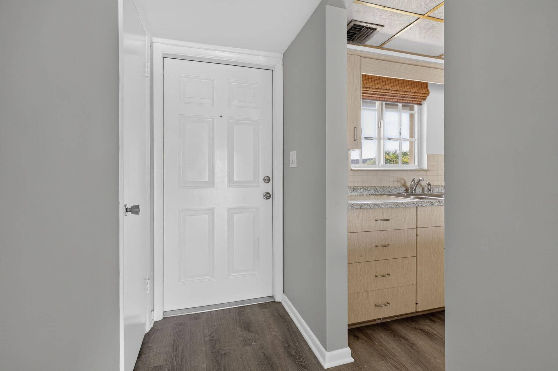 405 SOUTHWIND Drive, #3, North Palm Beach, FL 33408 Entryway featuring a solid six-panel door, wood-finish flooring, and neutral wall tones, revealing a kitchen area with flat-panel wood cabinetry, stone-texture countertops, and a double-pane window